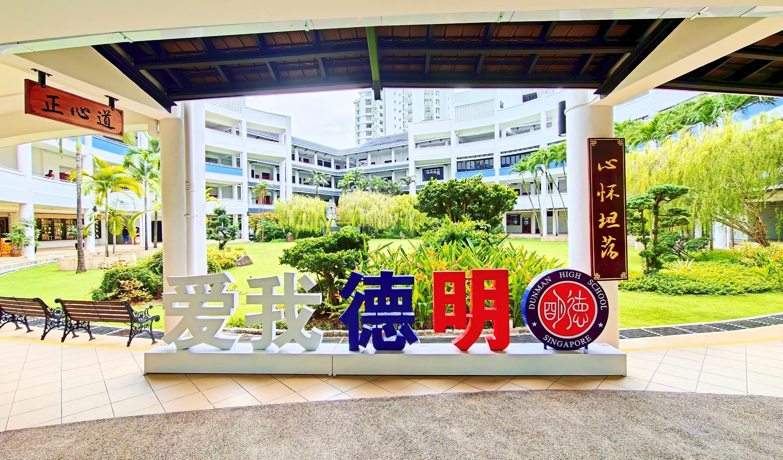 Dunman High School courtyard with the colourful “爱我德明” display, school crest and greenery.